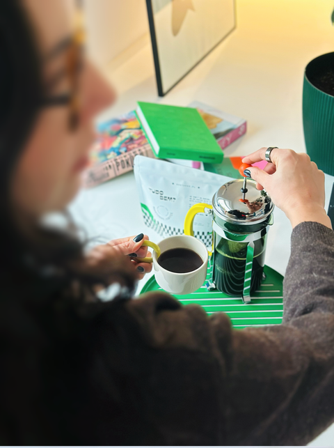Person making coffee using a manual grinder and filter, with a blurred background